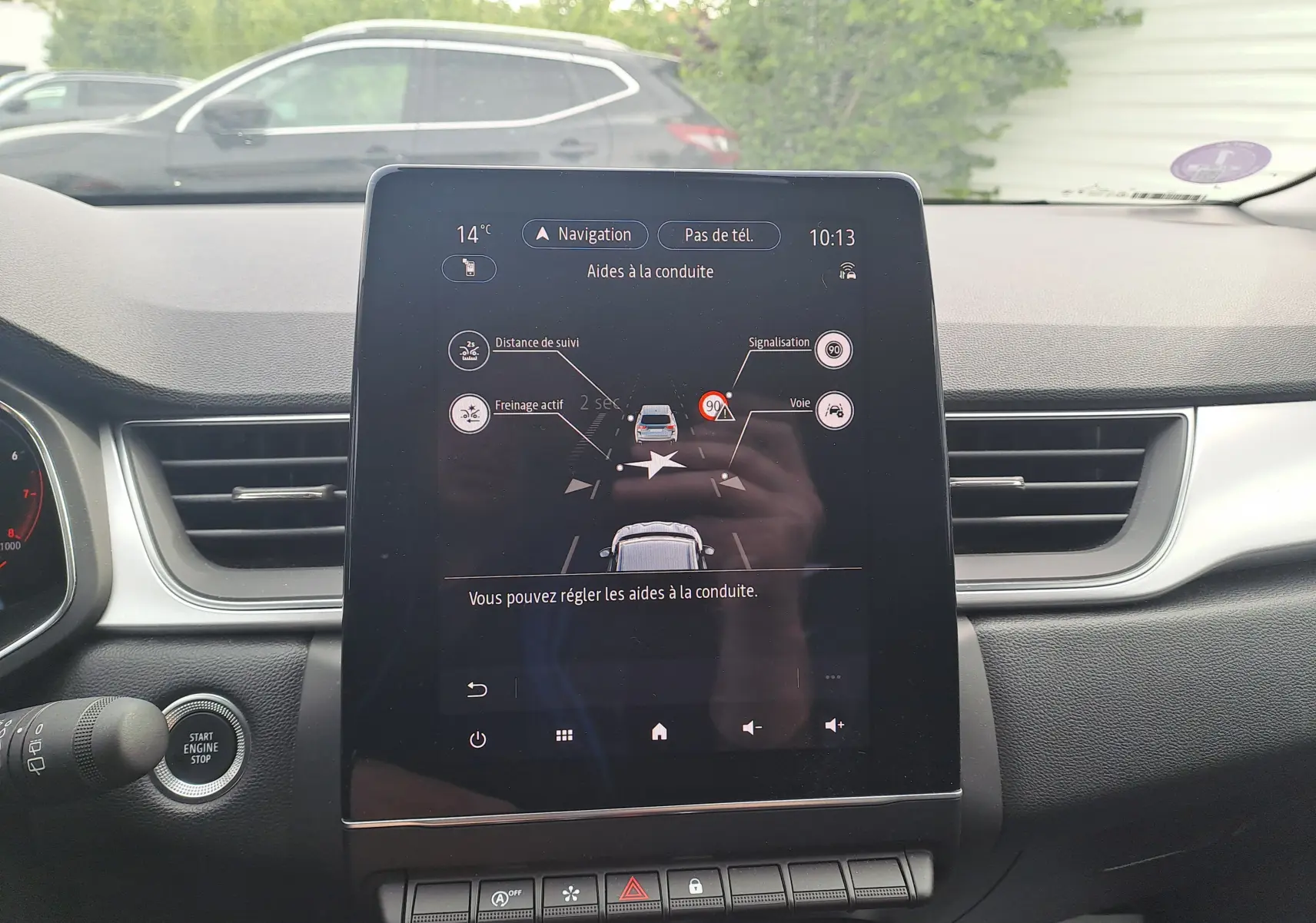 Vue intérieure centrée sur l’écran tactile du tableau de bord du Renault Captur gris cassiopée avec toit noir, affichant les aides à la conduite.