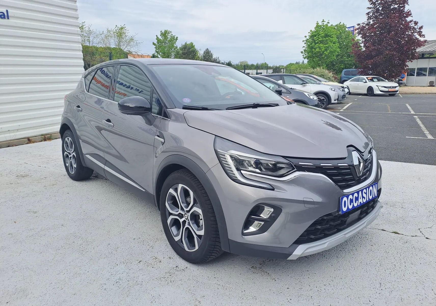 Renault Captur gris cassiopée avec toit noir, vue 3/4 avant droit, sur parking extérieur avec plaque occasion.