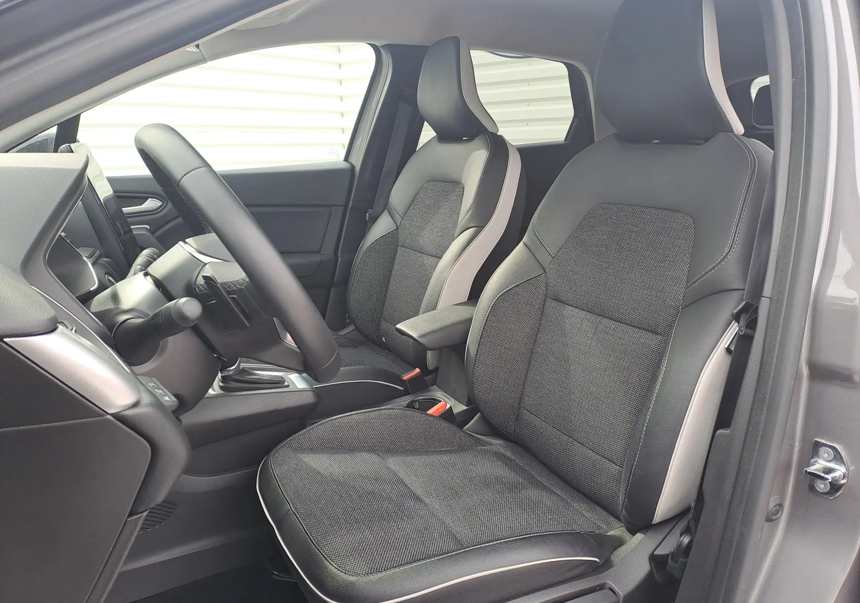 Vue intérieure côté conducteur du Renault Captur 2022, sièges tissu noir avec surpiqûres claires et garniture grise.