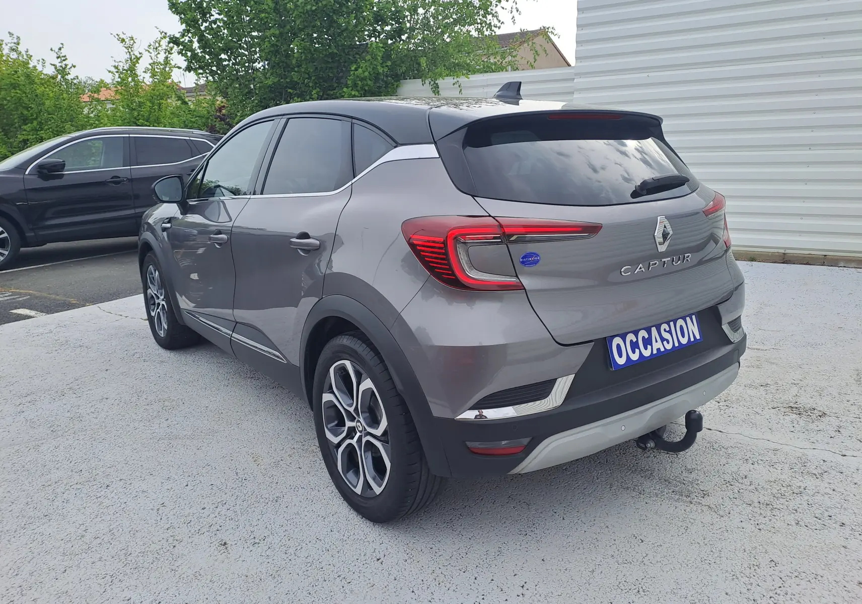 Vue 3/4 arrière droite du Renault Captur gris Cassiopée avec toit noir, feux LED et attelage visible.