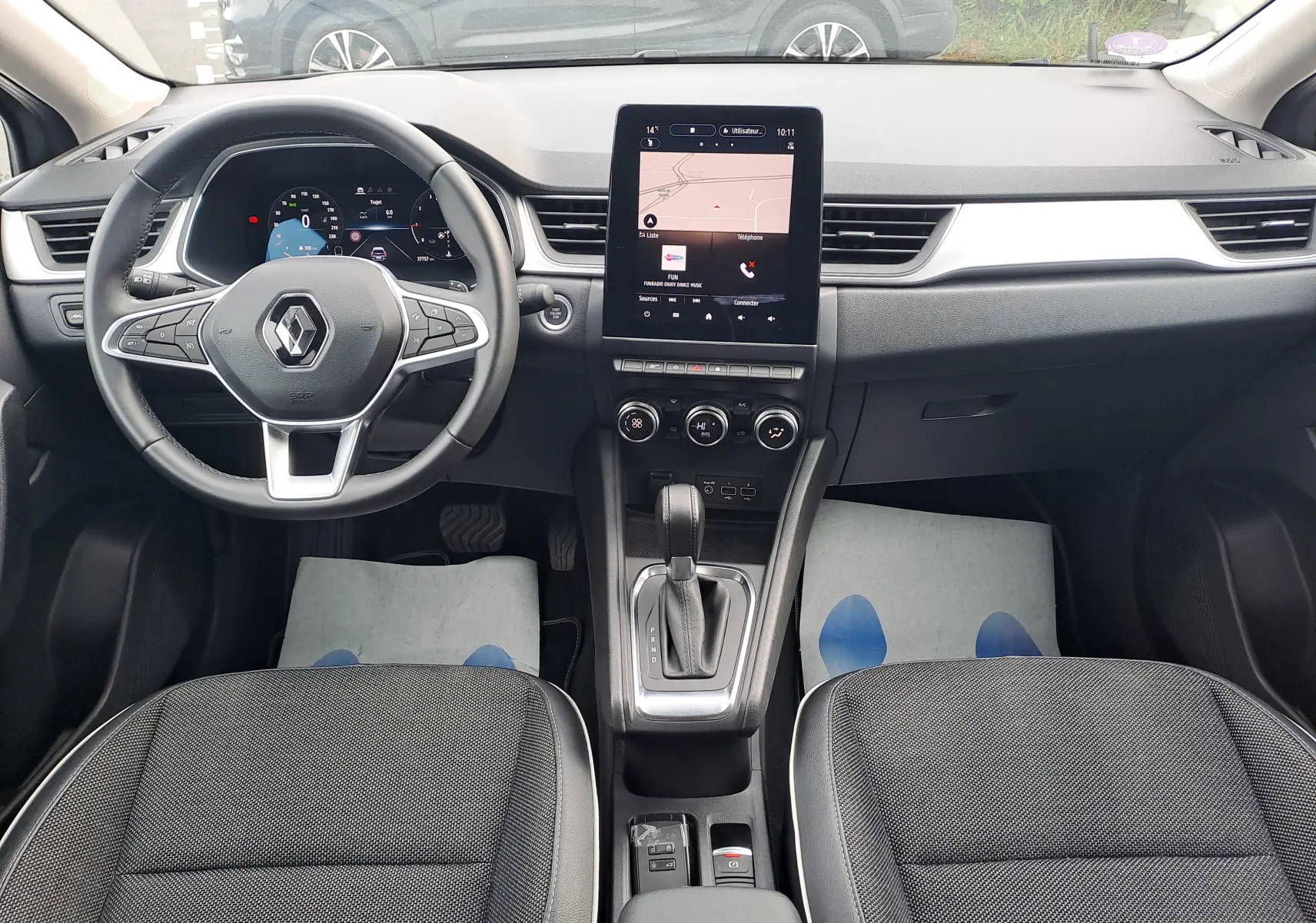 Vue intérieure frontale du tableau de bord et volant du Renault Captur 2022 avec écran tactile vertical et sellerie tissu gris.