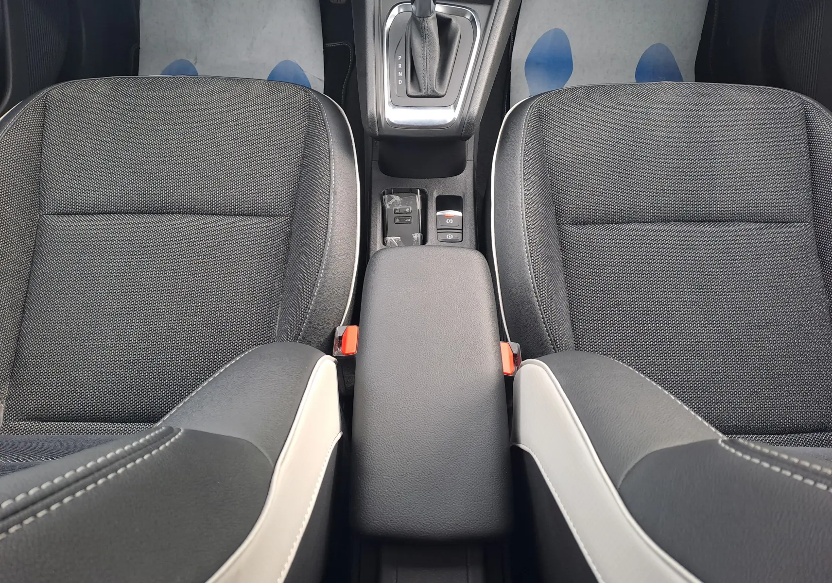 Vue intérieure centrée sur la console centrale et les sièges avant en tissu noir avec surpiqûres blanches du Renault Captur 2022.