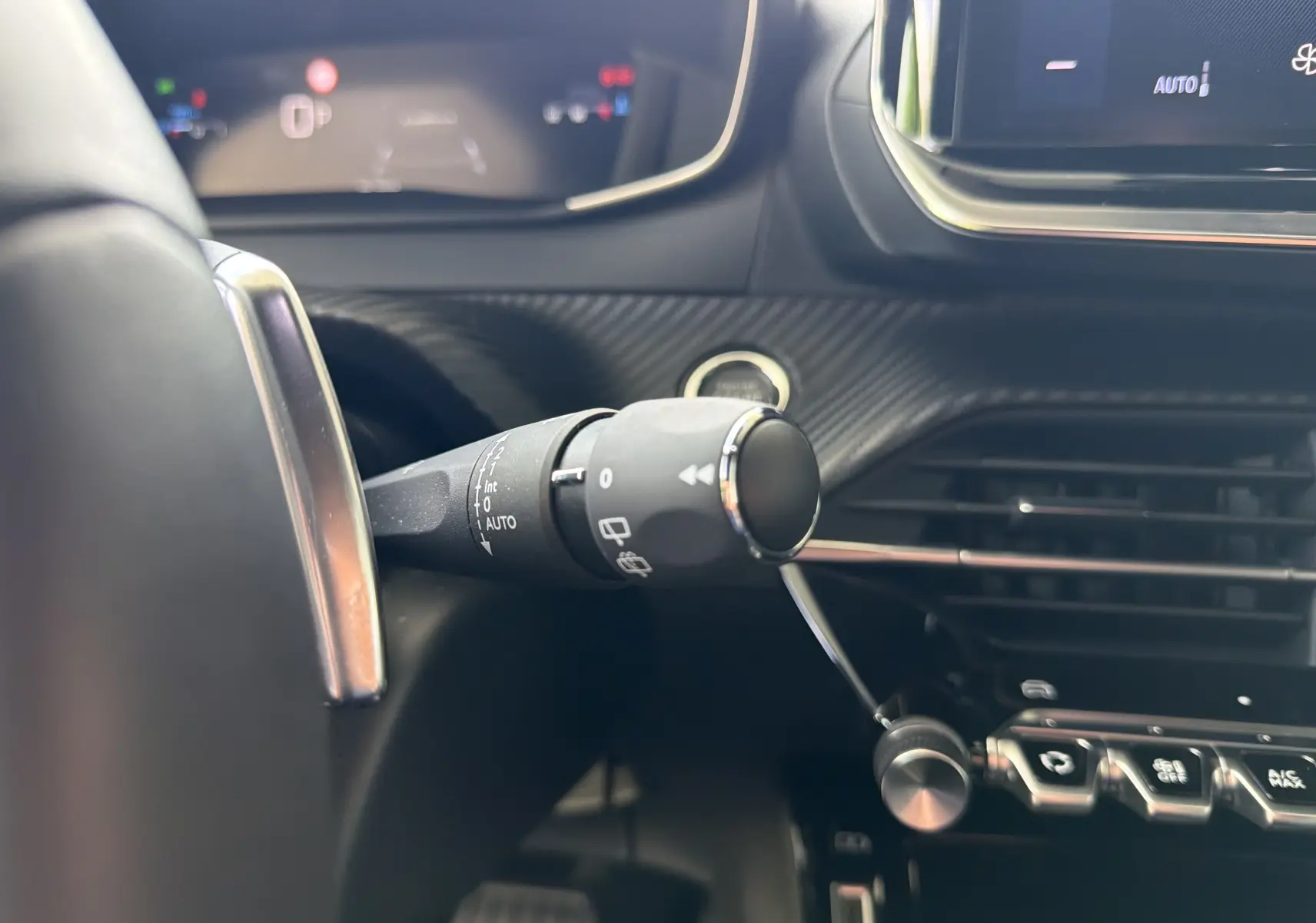 Gros plan intérieur sur la commande d’essuie-glace à gauche du volant du Peugeot 2008 gris Sellenium, avec tableau de bord numérique en arrière-plan.