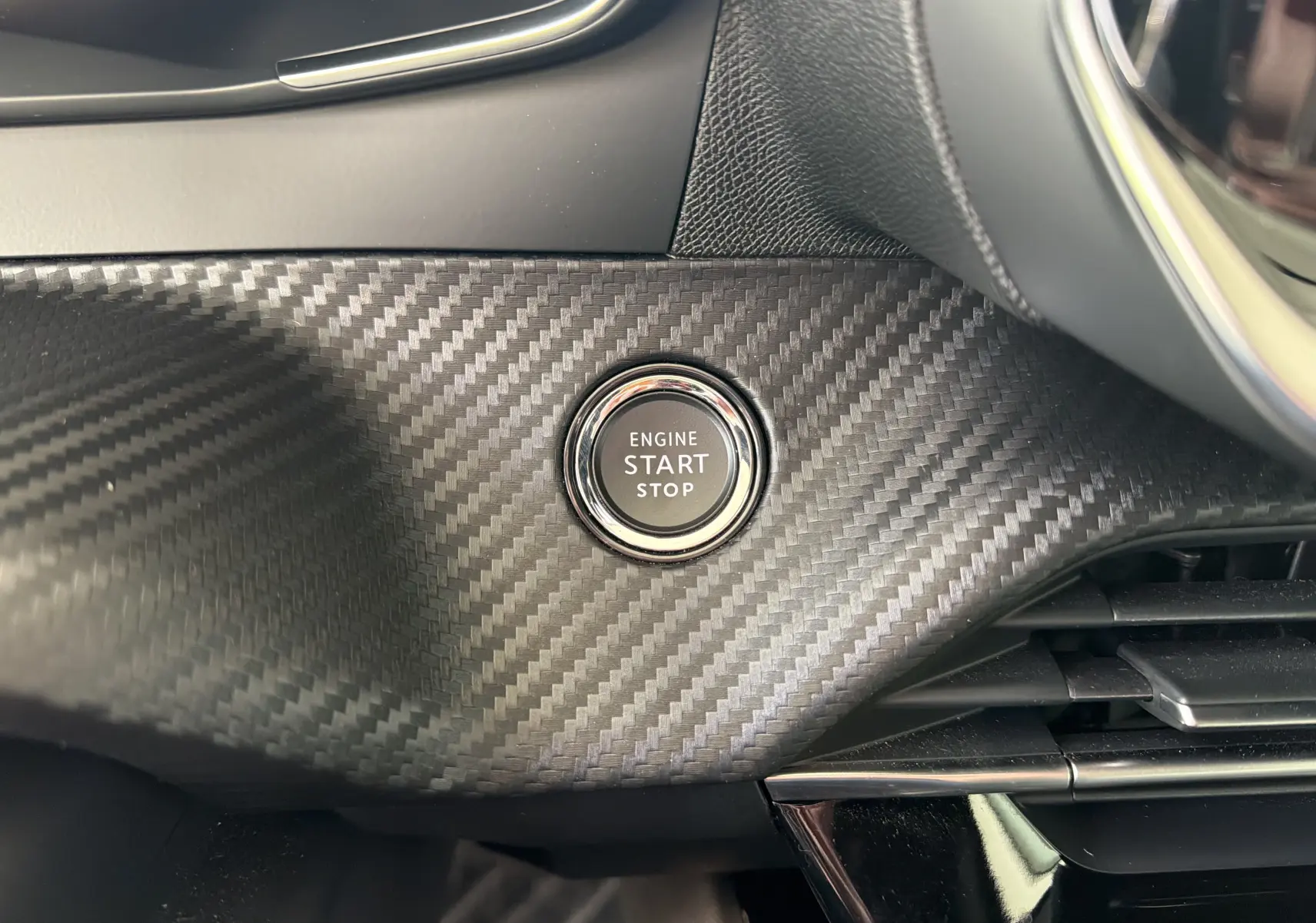 Détail intérieur du bouton start/stop sur tableau de bord effet carbone du Peugeot 2008 gris Sellenium 2023.