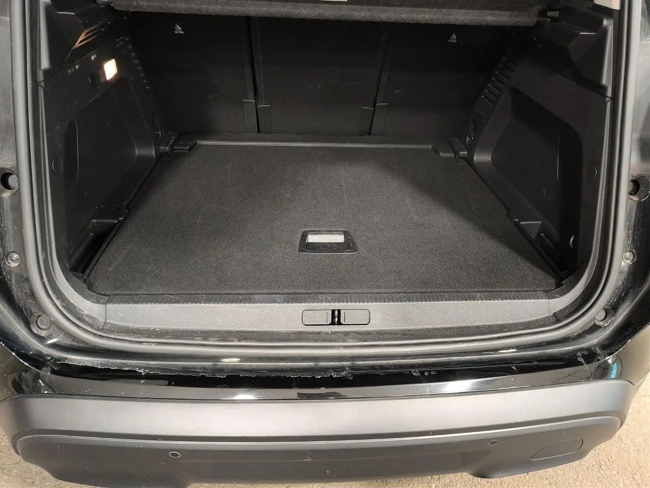 Coffre ouvert vu de l'arrière d'un Citroën C5 Aircross 2025 noir Perla avec seuil de chargement et éclairage intérieur.