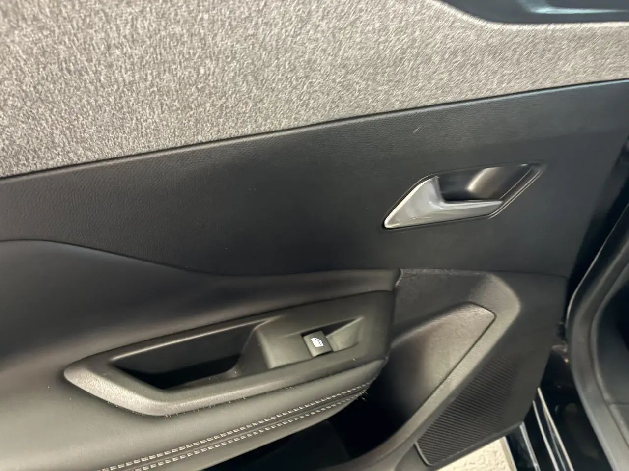 Gros plan sur la porte intérieure côté gauche noire avec poignée et commande de lève-vitre de la Peugeot 308 SW 2024.