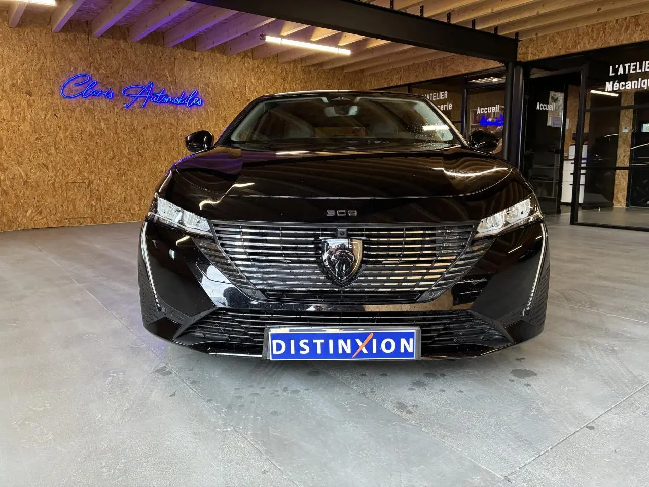 Vue avant d'une Peugeot 308 SW noire 2024 avec calandre chromée et logo lion au centre, en intérieur showroom.