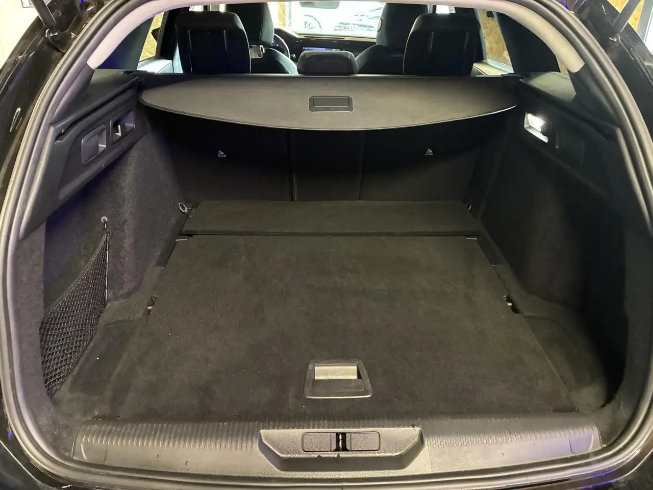 Coffre ouvert vu de l'arrière d'une Peugeot 308 SW noire avec cache-bagages et intérieur sombre.
