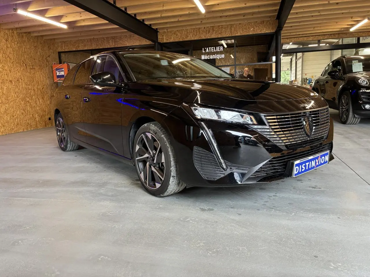 Peugeot 308 SW noire vue en 3/4 avant droit dans un garage avec jantes alliage et calandre chromée.