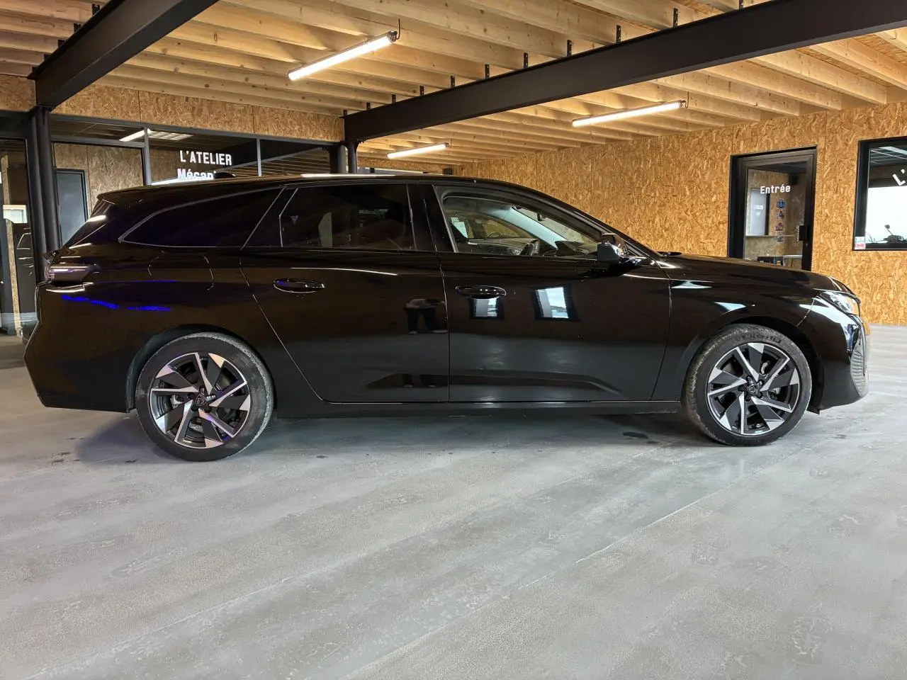 Peugeot 308 SW noire vue de profil côté gauche dans un garage avec jantes alliage et vitres surteintées.