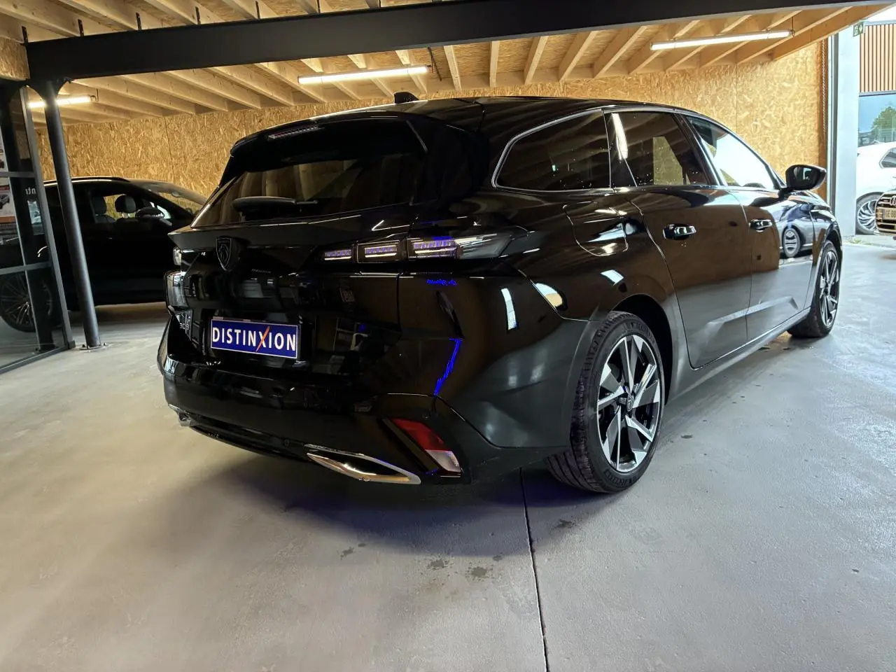 Peugeot 308 SW noire vue 3/4 arrière droit en intérieur avec jantes alliage et feux LED distinctifs.