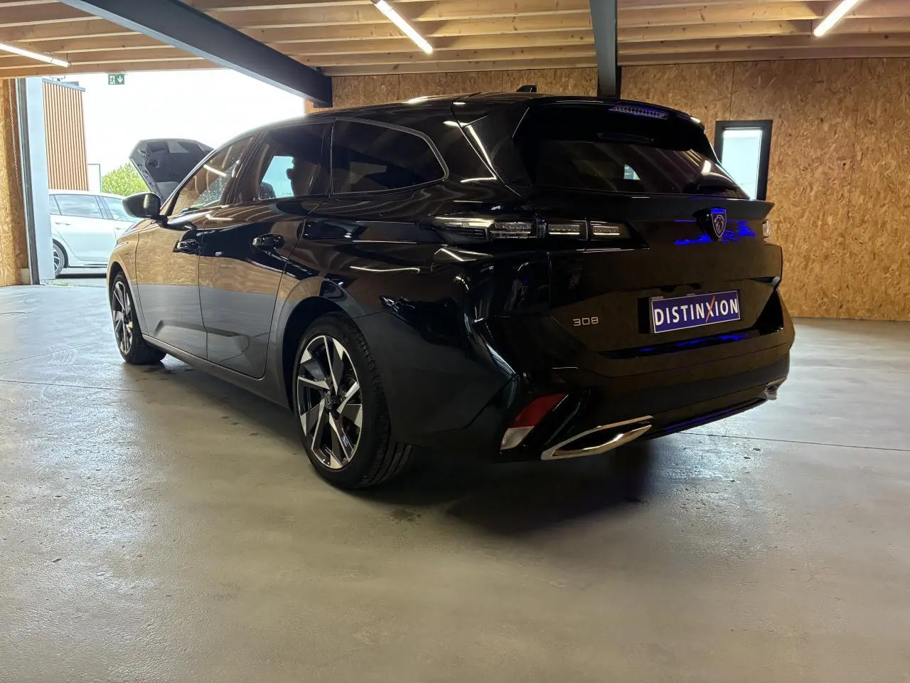 Peugeot 308 SW noire vue 3/4 arrière droit dans un garage, avec feux arrière LED et jantes alliage 17 pouces.
