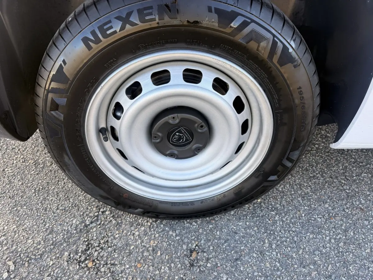 Gros plan sur la roue avant droite du Peugeot Partner blanc, avec jante acier et logo Peugeot au centre.