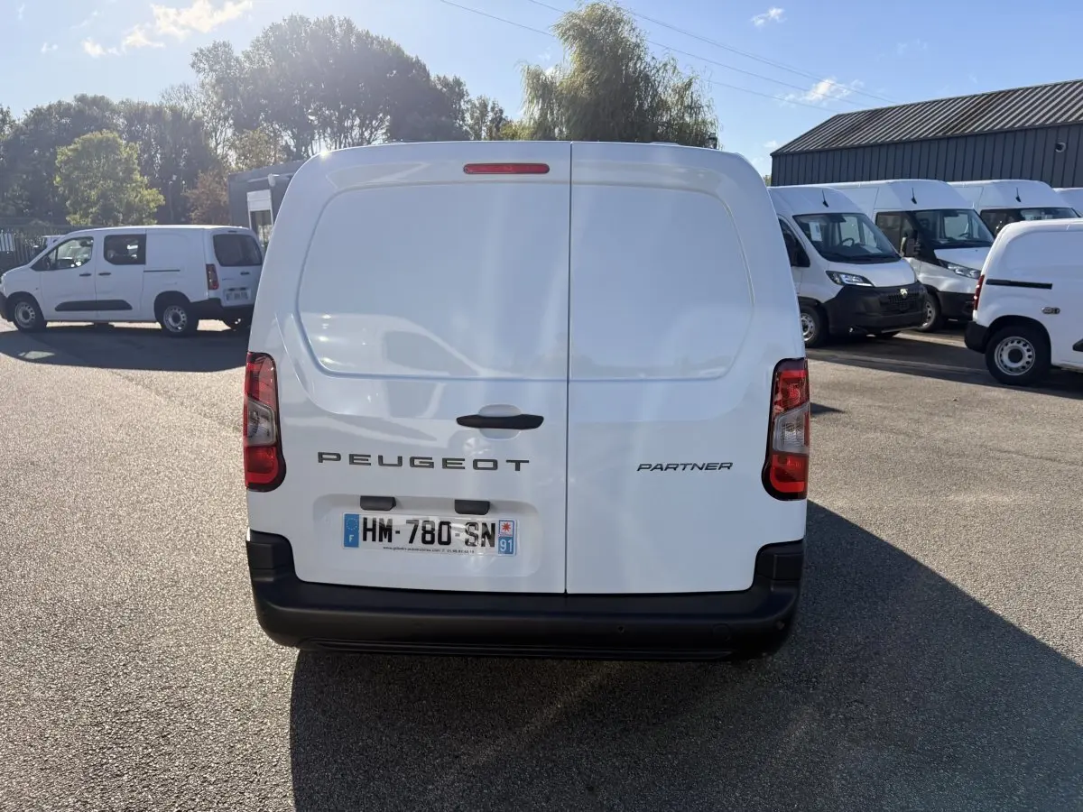 Vue arrière d’un utilitaire blanc Peugeot Partner Taille M, portes battantes fermées, plaque d’immatriculation visible.