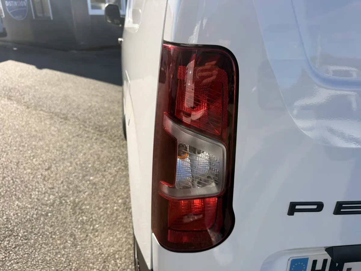 Gros plan sur le feu arrière droit d’un Peugeot Partner blanc, avec partie arrière et logo partiel visibles.