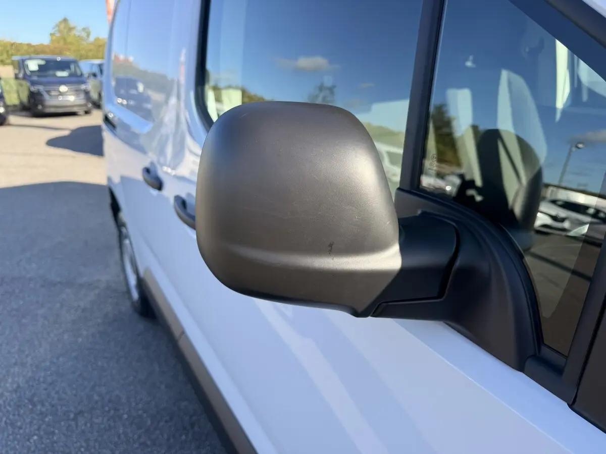 Vue rapprochée du rétroviseur côté conducteur d’un Peugeot Partner blanc, avec reflet du ciel bleu sur la carrosserie.
