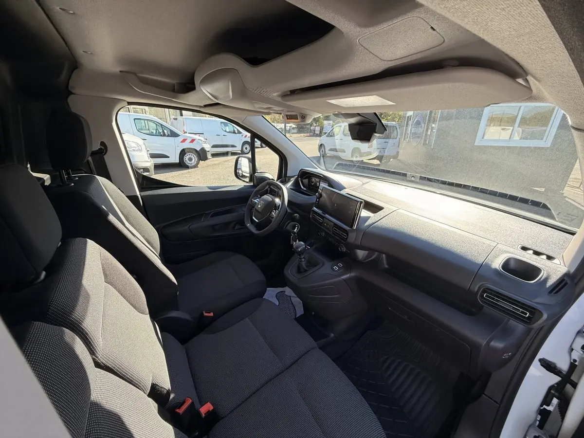 Vue intérieure côté conducteur du Peugeot Partner blanc, montrant le tableau de bord et les sièges avant noirs.