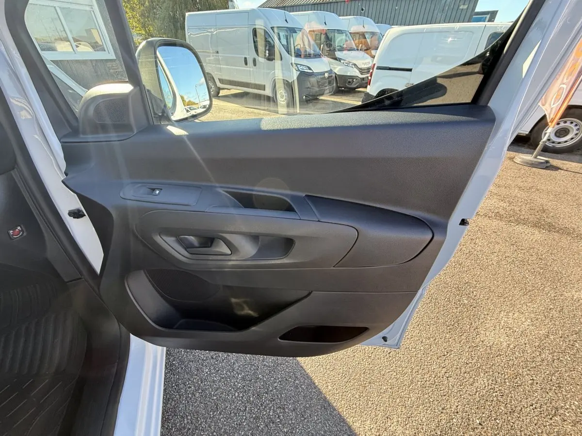 Vue intérieure de la porte côté conducteur du Peugeot Partner blanc, avec poignée et commande de vitre visible.
