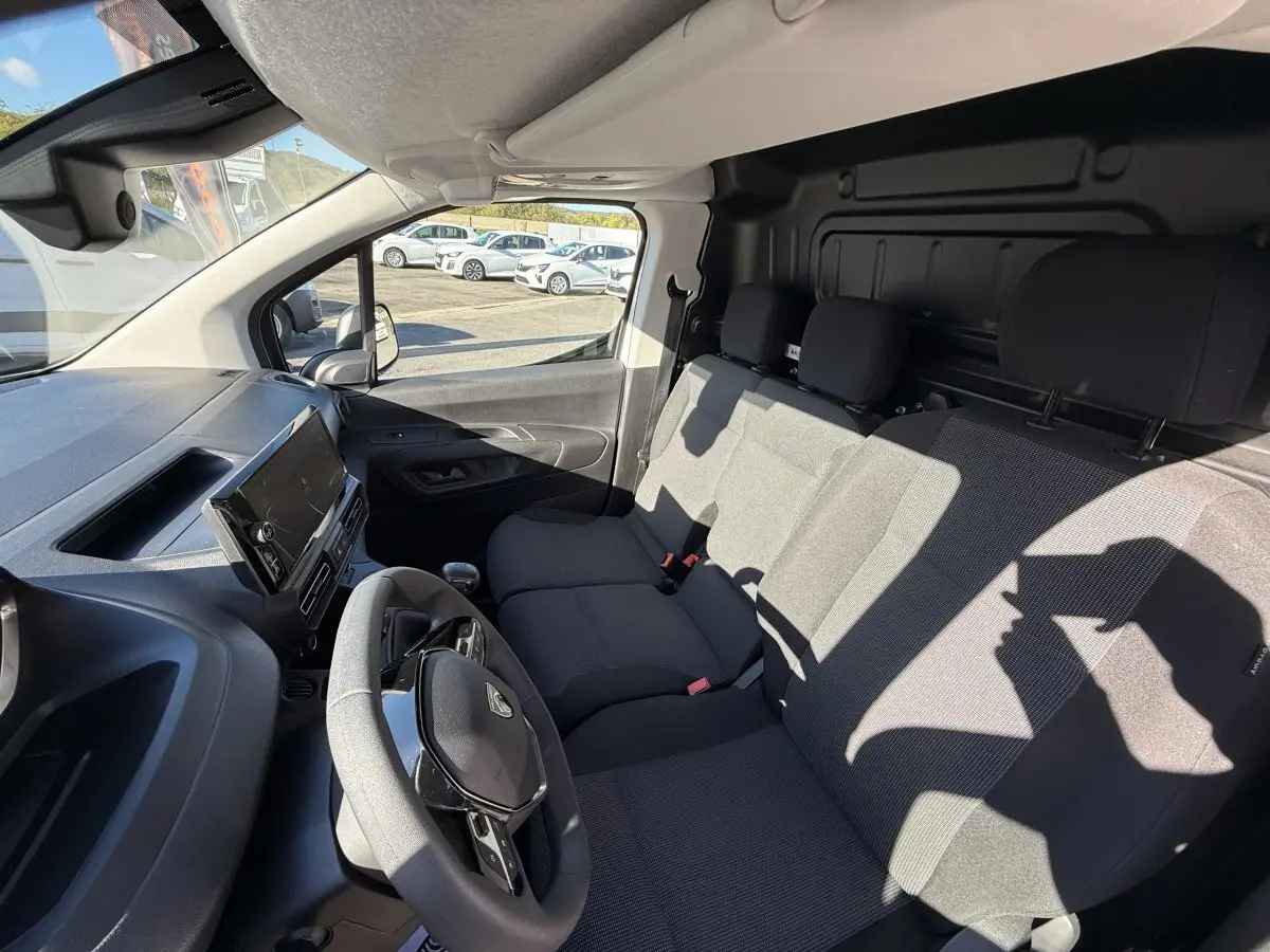 Vue intérieure avant droite du Peugeot Partner blanc 2026, montrant le volant multifonctions et la banquette trois places.