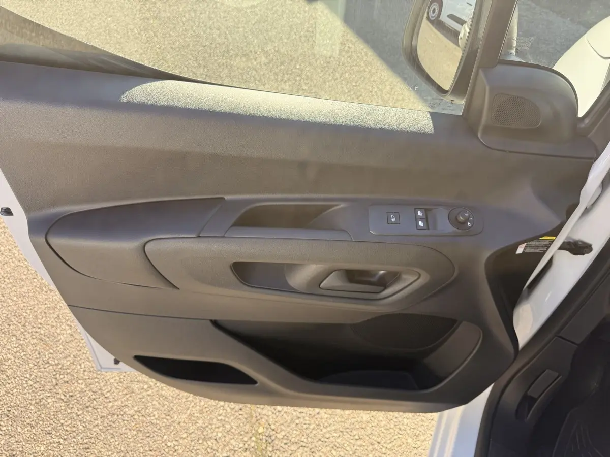 Vue intérieure de la porte avant gauche noire du Peugeot Partner blanc, avec commandes électriques des vitres et rétroviseurs.