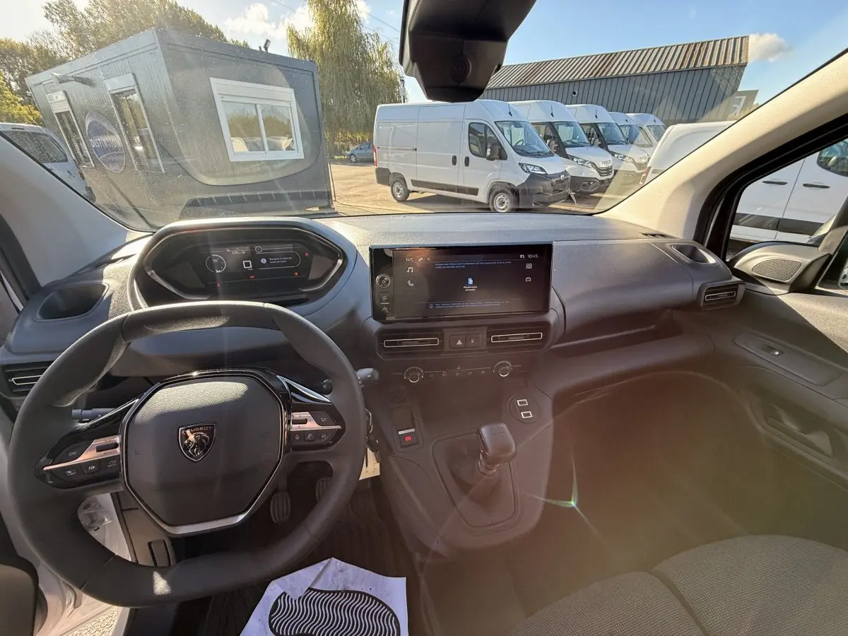 Vue intérieure du poste de conduite du Peugeot Partner blanc 2026, avec volant multifonctions et écran tactile central.