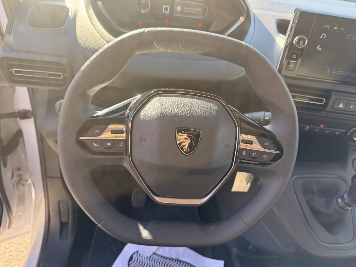 Vue rapprochée du volant multifonctions noir avec logo Peugeot au centre dans l'habitacle du Partner blanc 2026.