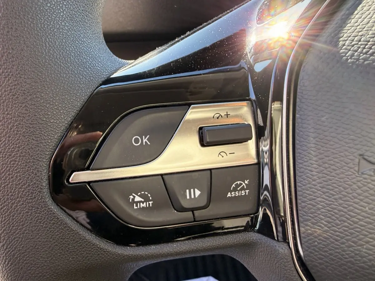 Gros plan sur les commandes noires et argentées du volant multifonctions du Peugeot Partner blanc, côté gauche.