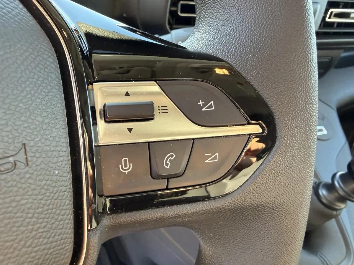 Gros plan sur les commandes multifonctions noires et argentées du volant du Peugeot Partner blanc, côté gauche.