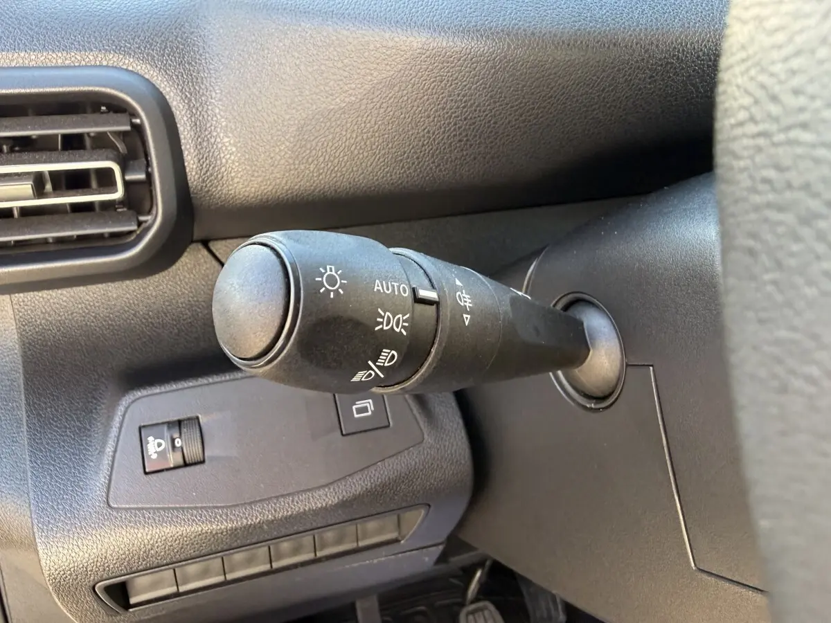 Gros plan sur la commande des phares à gauche du volant dans l’habitacle noir du Peugeot Partner blanc.
