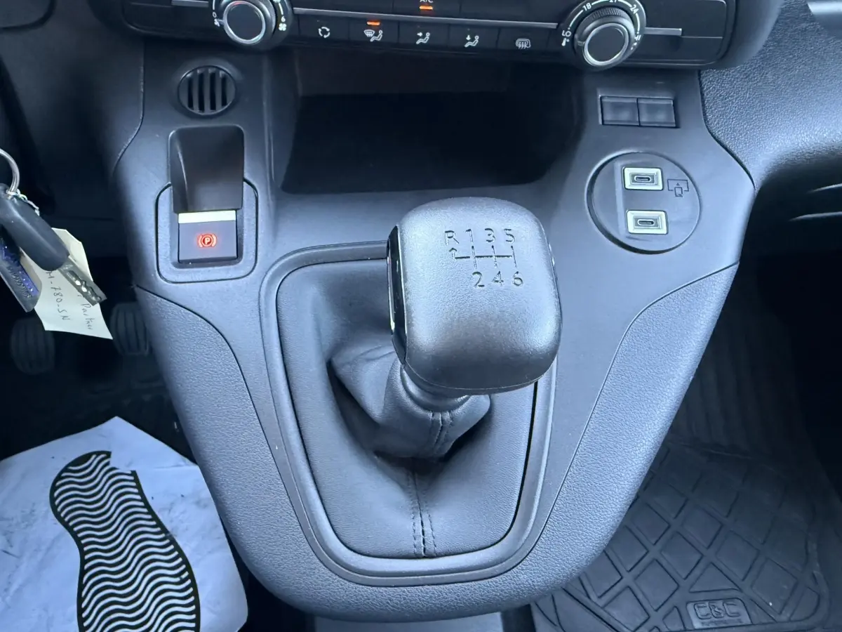 Gros plan intérieur sur le levier de vitesses manuel noir du Peugeot Partner blanc, avec ports USB et frein à main électrique.