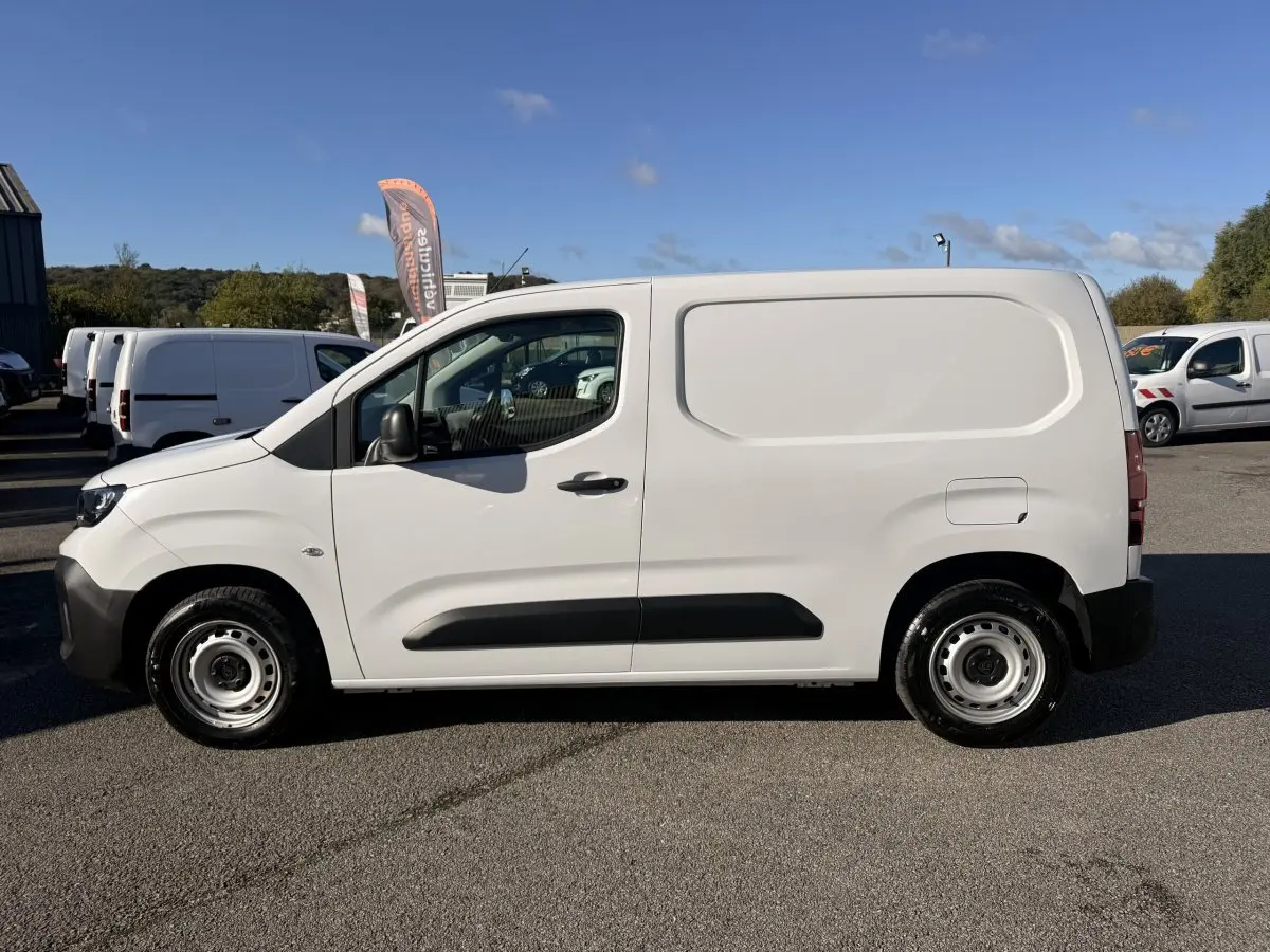 Vue de profil côté gauche d’un utilitaire Peugeot Partner blanc avec protections latérales noires sur un parking.