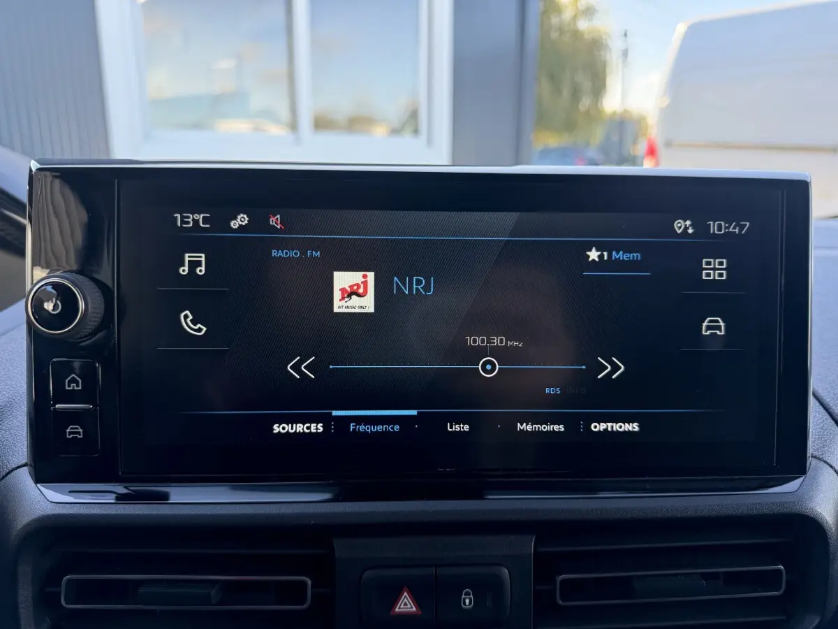 Écran tactile central du Peugeot Partner 2026 affichant la radio NRJ en FM, avec commandes tactiles sur le côté gauche.