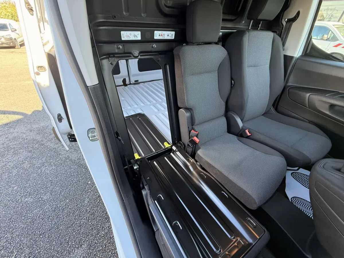 Intérieur du Peugeot Partner blanc, vue côté droit sur les sièges avant et cloison pleine avec ouverture vers la zone de chargement.