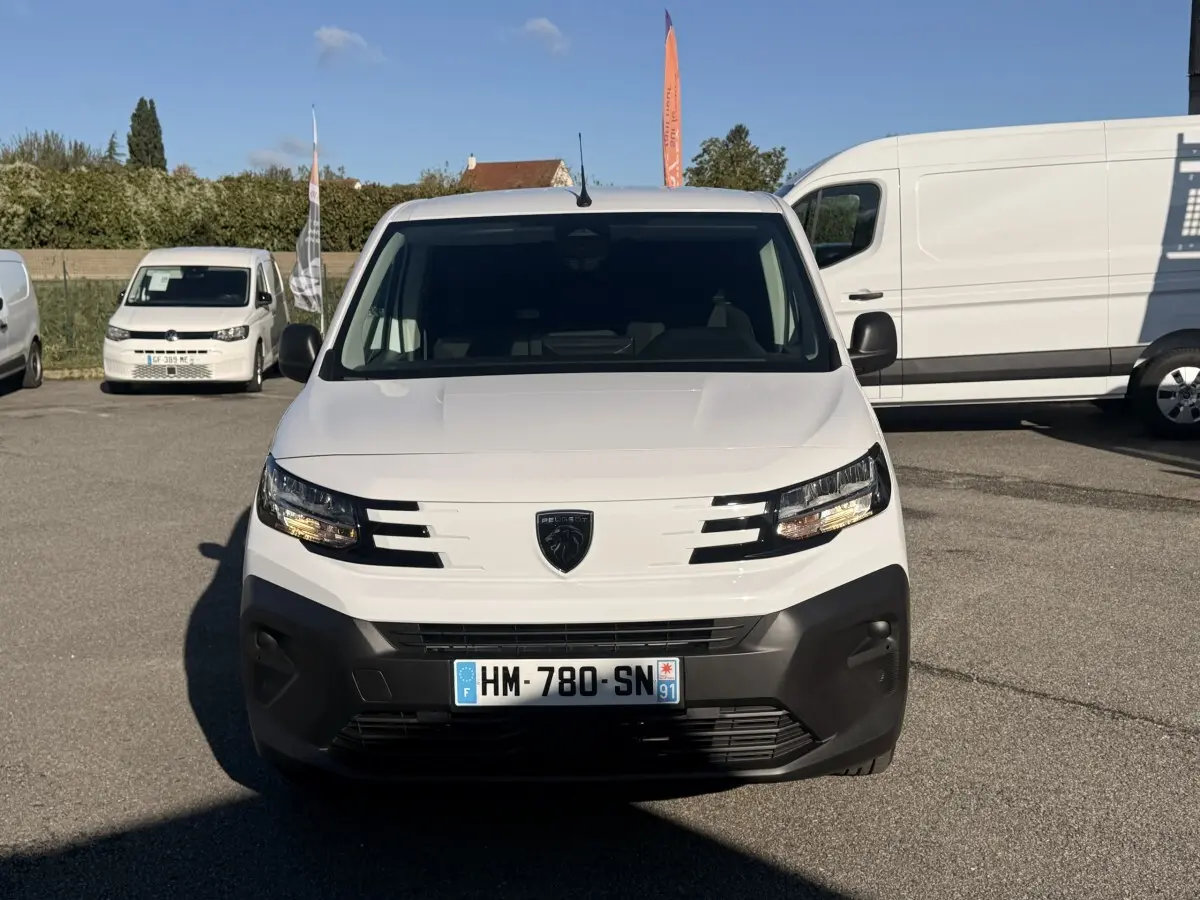 Vue de face d'un Peugeot Partner blanc avec pare-chocs noir, sur un parking en extérieur.