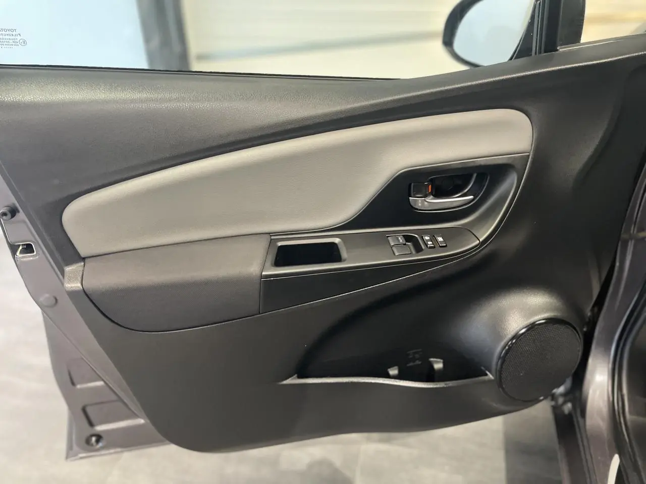 Porte avant gauche ouverte d'une Toyota Yaris hybride gris foncé, avec commandes de vitres et haut-parleur intégré.