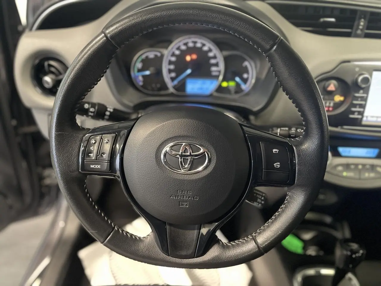 Vue rapprochée du volant en cuir noir de la Toyota Yaris hybride 2020, avec commandes intégrées et tableau de bord flou en arrière-plan.