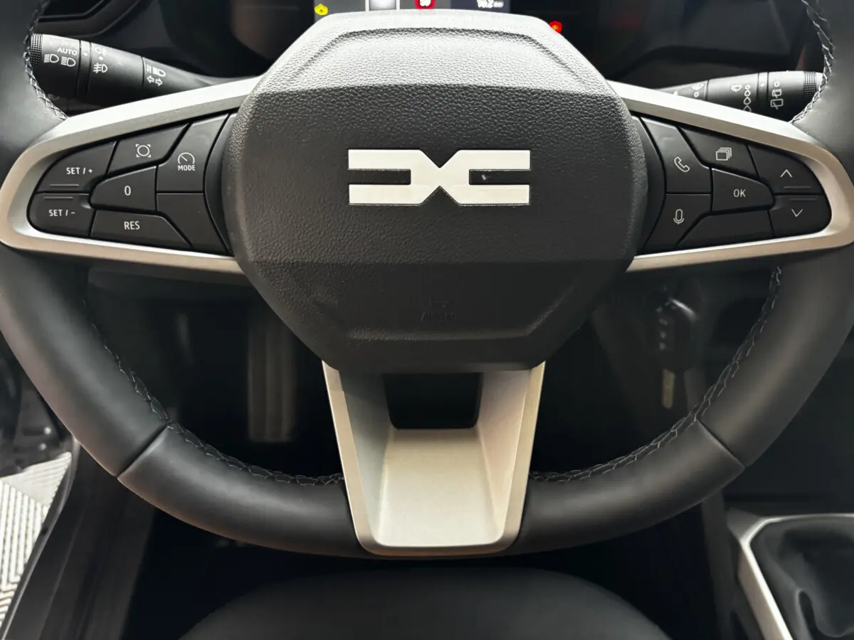Gros plan sur le volant cuir noir du Dacia Bigster 2025 avec commandes multifonctions et logo central gris.
