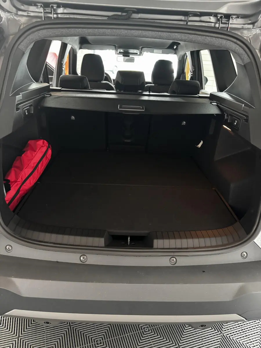 Coffre ouvert du Dacia Bigster gris foncé, vue arrière montrant la banquette arrière et un sac rouge à gauche.