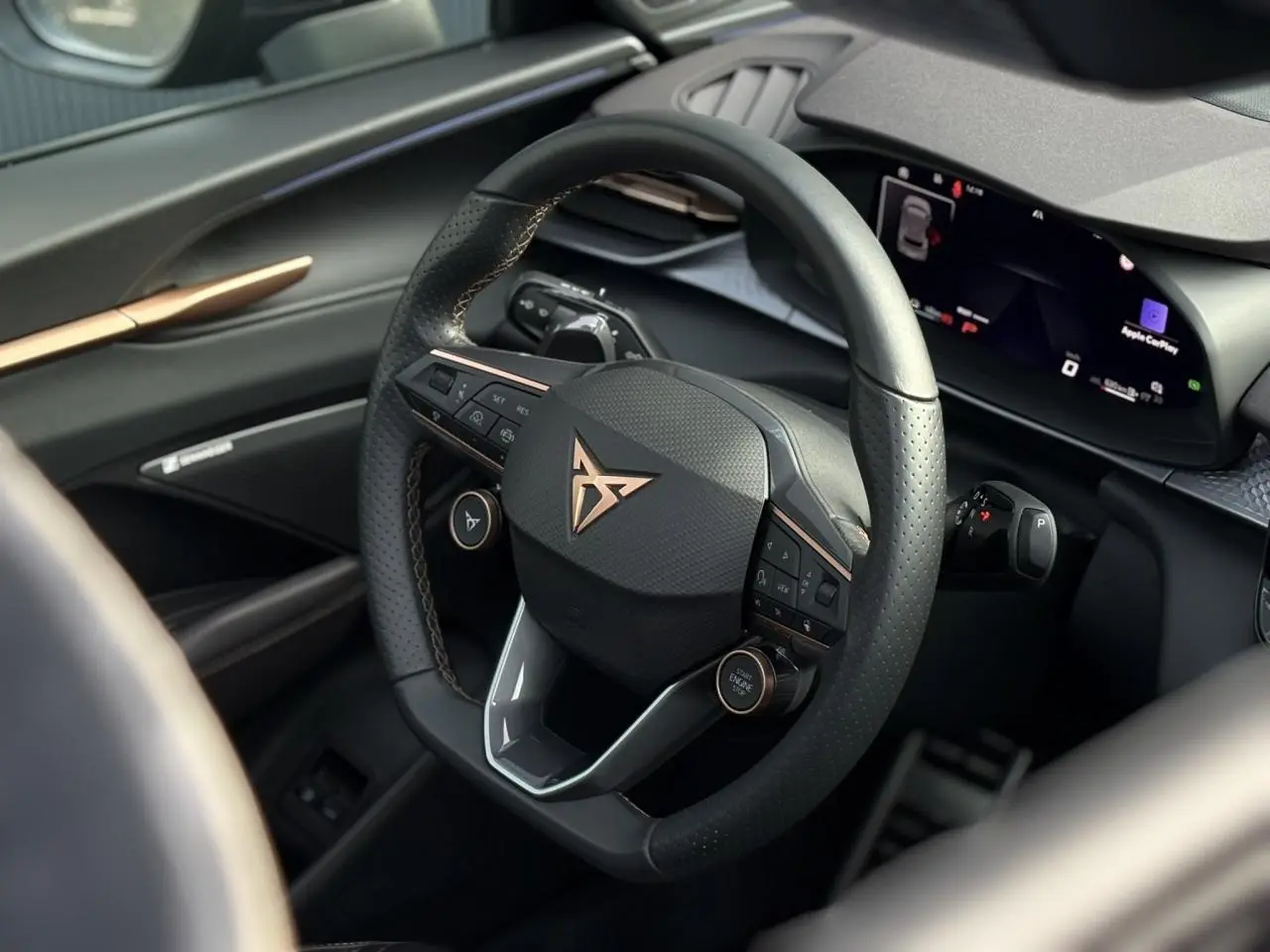 Vue rapprochée du volant cuir noir perforé avec logo cuivré et tableau de bord numérique du CUPRA Terramar 2024.