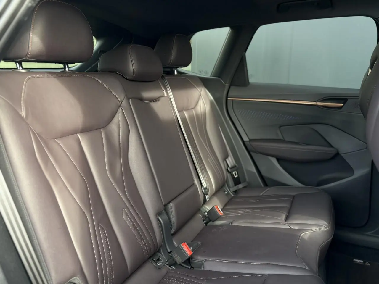 Vue latérale droite des sièges arrière en cuir marron foncé du CUPRA TERRAMAR 2024 avec détails cuivrés sur la porte.