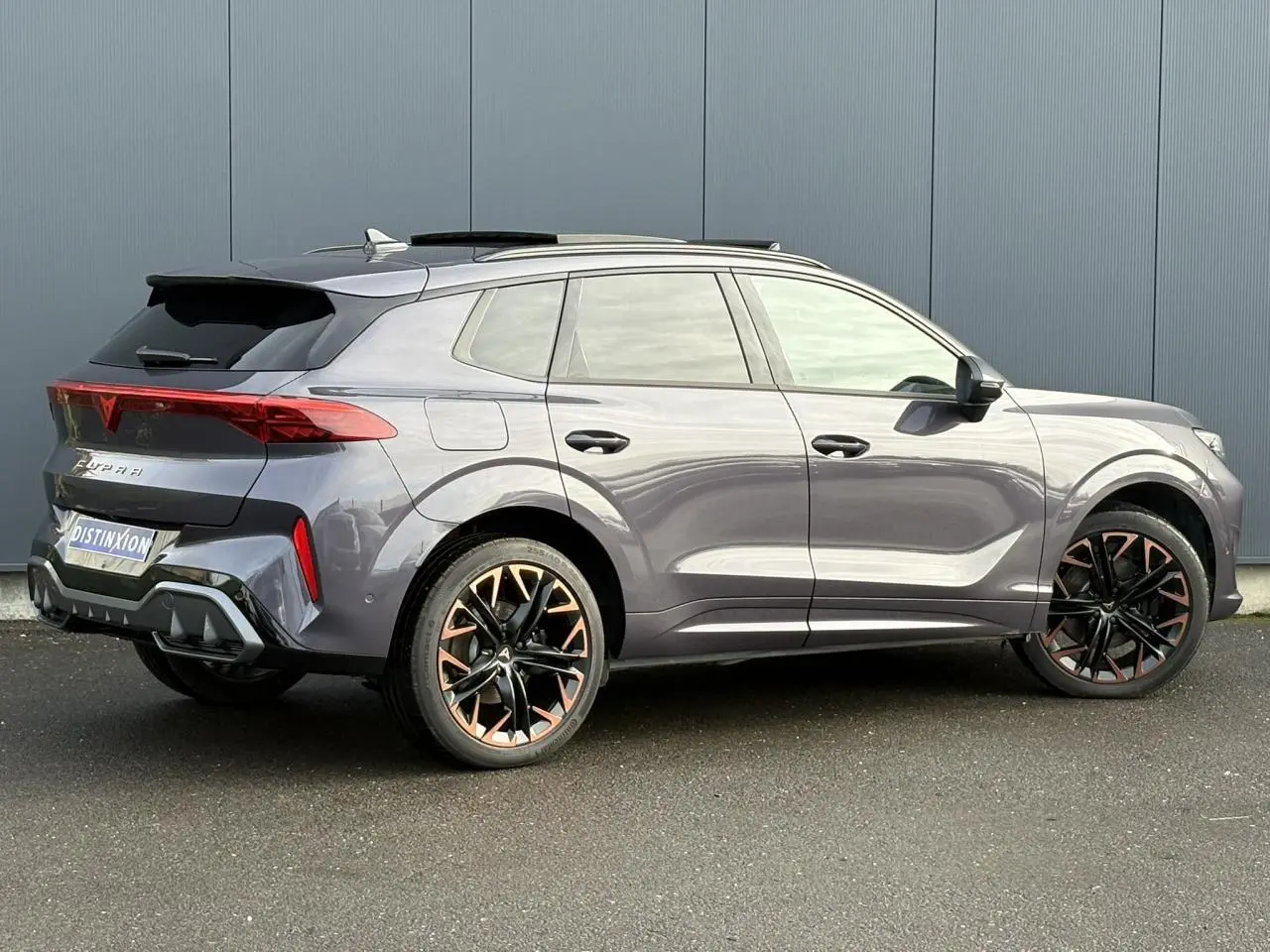 Vue 3/4 arrière droite de la CUPRA TERRAMAR 1.5 e-Hybrid gris Dark Void avec jantes cuivrées et toit ouvrant.
