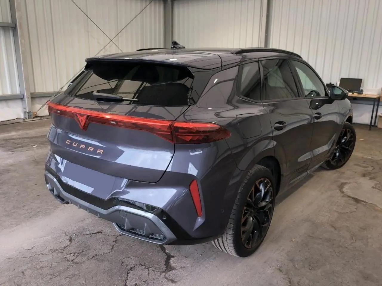 Vue 3/4 arrière droite du CUPRA TERRAMAR 2024 Dark Void avec jantes cuivrées et hayon électrique en intérieur d'atelier.