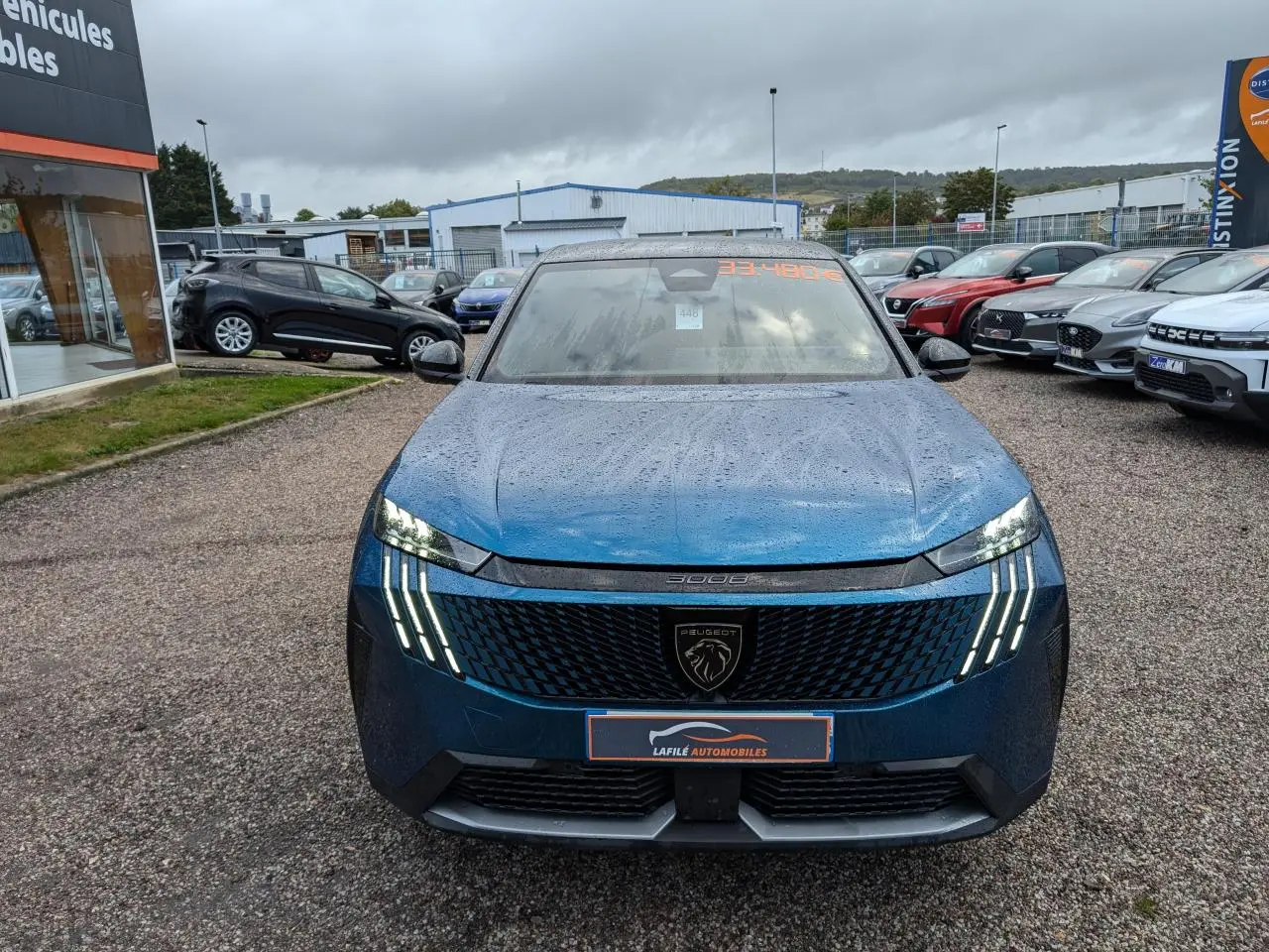 Vue avant d'un Peugeot 3008 GT bleu métallisé avec feux LED griffes et calandre noire laquée sous un ciel nuageux.