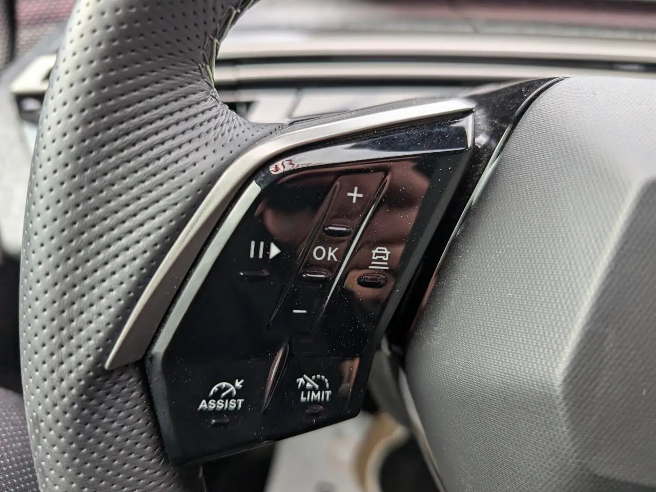 Gros plan sur les commandes noires du volant perforé côté gauche du Peugeot 3008 GT bleu métallisé 2025.