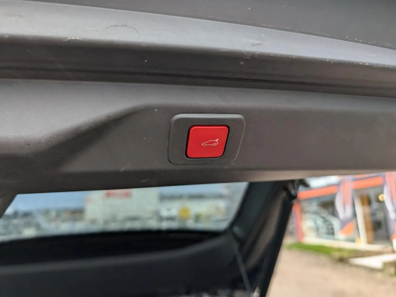 Bouton rouge d'ouverture électrique du hayon visible en gros plan sur un Peugeot 3008 hybride 2025.