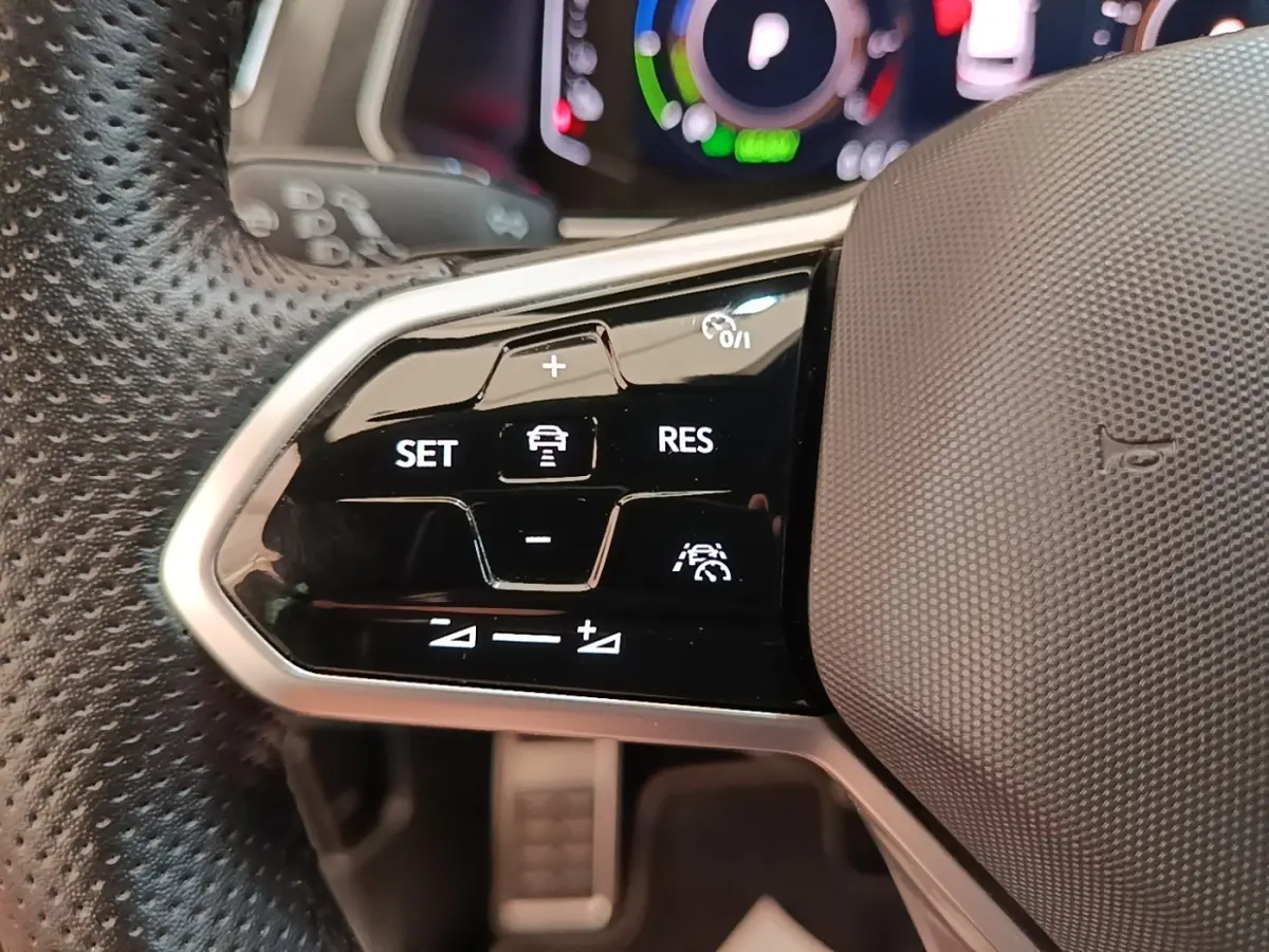 Gros plan sur les commandes de régulateur de vitesse au volant cuir perforé du Volkswagen Tiguan blanc 2023.