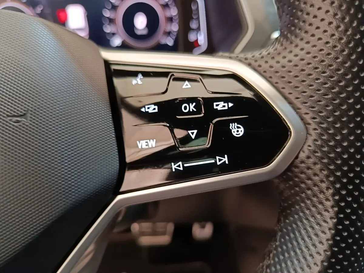 Gros plan sur les commandes multifonctions noires du volant perforé du Volkswagen Tiguan blanc 1.4 eHybrid 2023.