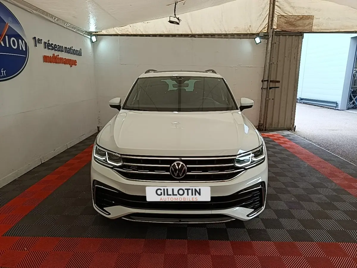 Vue avant d'un Volkswagen Tiguan blanc 2023 en version R-Line, avec phares LED allumés dans un garage.
