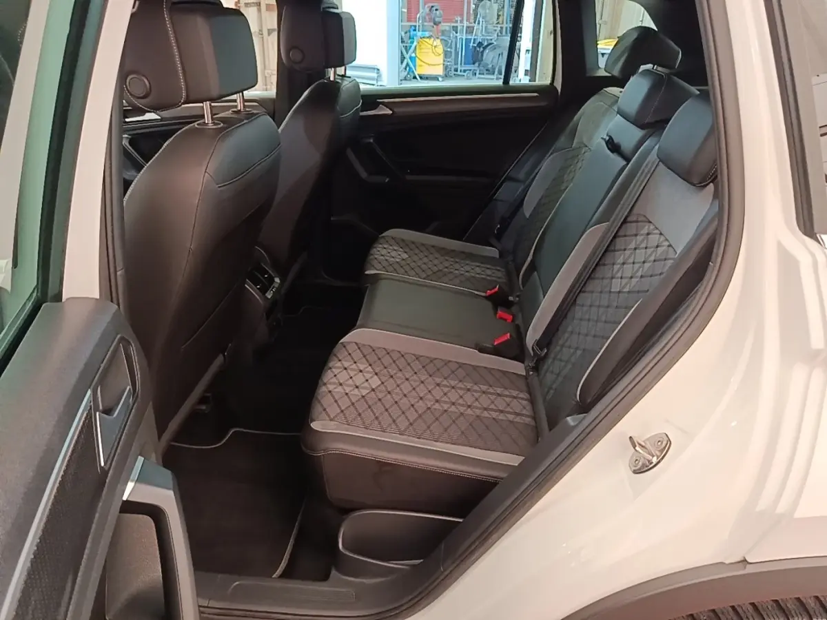 Vue intérieure côté arrière droit du Volkswagen Tiguan blanc 2023, sièges arrière en cuir et tissu gris à motifs.