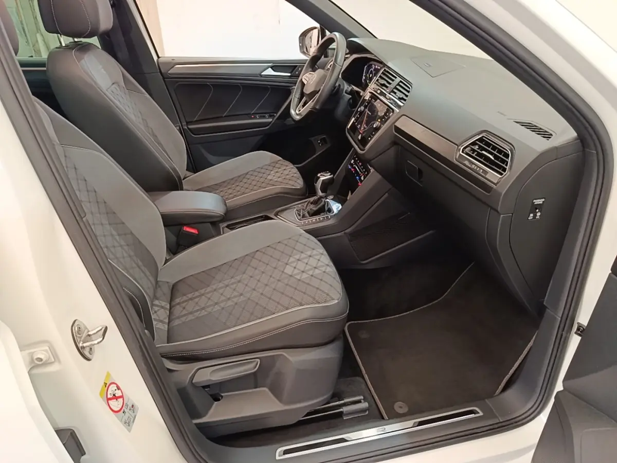 Intérieur avant droit du Volkswagen Tiguan blanc 2023, sièges tissu gris à motifs, tableau de bord moderne avec écran tactile.